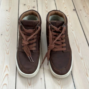 Bruna sneakers från Björn Borg - Säljer ett par bruna sneakers från Björn Borg med snörning och vit platt sula. Skorna har rund tå och är tillverkade i skinn med mjukt foder på insidan. Perfekta för dig som gillar en klassisk och stilren look.