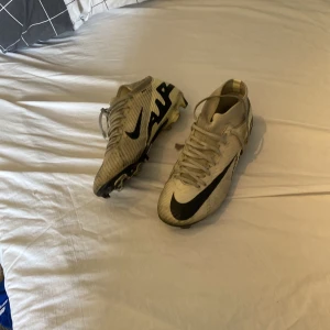 Nike Zoom fotbollsskor i beige och svart - Säljer ett par Nike Zoom fotbollsskor i beige med svarta detaljer och snörning. Skorna har platt sula med dobbar för bra grepp på planen och en sportig design med stor Nike-logga på sidan.