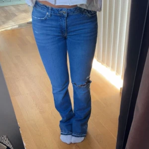 Blå bootcut jeans med slitning - Säljer ett par klassiska blå jeans med bootcut passform och en snygg slitning vid knät. 