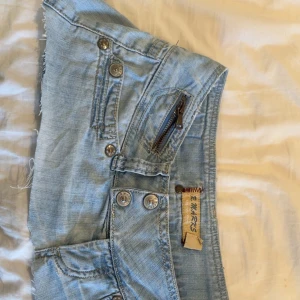 Jeanskjol  - Ljusblå jeanskjol med flera fickor, dekorativ dragkedja och råa, fransiga benslut. Shortsen har knappgylf och synliga sömmar för en cool look. Perfekta för varma dagar.secondhand 