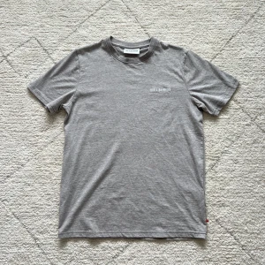 Grå t-shirt från Han Kjøbenhavn - Säljer en stilren grå t-shirt från Han Kjøbenhavn med diskret broderad logga på bröstet. T-shirten har rund halsringning och är tillverkad i mjuk bomull. Perfekt för en clean och enkel look. Retail: 59€