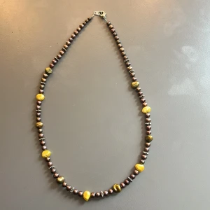 Halsband med bruna och gula pärlor - Handgjort halsband med skimrande bruna pärlor och oregelbundna gula pärlor. Mellan pärlorna finns små silvriga detaljer som ger extra karaktär. 