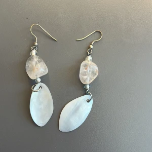 Handgjorda örhängen med stenar och pärlemor - Handgjorda örhängen med oregelbundna, genomskinliga stenar och stora, vita pärlemorliknande hängen. Krokar i metall. 
