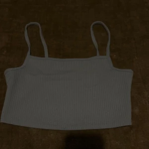 Ljusgrå ribbad crop top - Säljer en ljusgrå ribbad crop top med smala axelband. Toppen är croppad och har en enkel, stilren design som passar perfekt till sommaren. Den är köpt ifrån bershka🤍