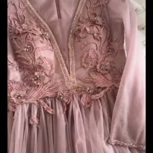 Lilla Rosa långklänning med broderade detaljer - Säljer en romantisk långklänning i lilla rosa med v-ringning och vackra broderade blommor och pärlor upptill. Klänningen har långa, transparenta ärmar och ett svepande, voluminöst kjolparti i tunt material. Använd bara en gång, jag köpte på 2500 kr. storlek mellan 38_40 