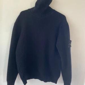 Svart stickad polotröja från Stone Island - Säljer en svart stickad polotröja från Stone Island med klassisk patch på ärmen. Tröjan har hög      polokrage och ribbade muddar. Perfekt för dig som   gillar stilrena och varma plagg med streetkänsla.  