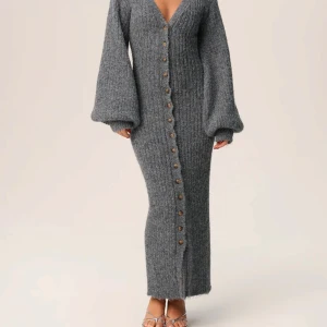 Adoore Montana dress  - Mysig grå långklänning i stickat material med v-ringning och stora ballongärmar. Klänningen har knappar hela vägen framtill och kan även bäras öppen som en lång kofta. Perfekt för lager-på-lager-stil.