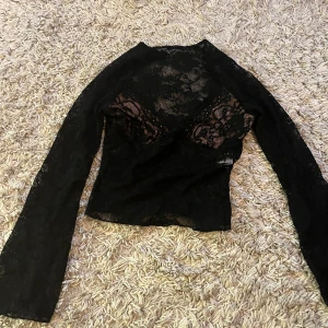 Svart spetsblus med lång ärm - Säljer en svart blus i genombruten spets med lång ärm. Blusen har ett blommigt spetsmönster och är figurnära i modellen och urringad. Oanvänd då den inte riktigt passade i storlek. Vet ej varumärke då den är köpt på Vinted