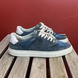 Blå och grå sneakers från Jacob Cohën - Snygga sneakers från Jacob Cohën i blått och grått med vita snören och vit sula. Ovandelen är i en mix av mocka och jeansmaterial, med rund tå och platt sula. 28,5cm innersula-