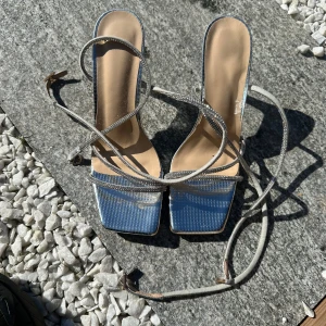 Glittriga silverfärgade sandaler med transparent klack - Säljer ett par sandaler med glittriga silverremmar och fyrkantig tå. Skorna har transparent klack och tunna remmar som går att snöra runt vristen. Perfekta för dig som vill sticka ut lite extra.
