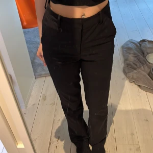 Svarta kostymbyxor med bootcut - Snygga svarta kostymbyxor med bootcut passform och hög midja. Byxorna har klassiska fickor och stängs med dragkedja och knapp framtill. Perfekta för en stilren look. De är i stl 34 men skulle uppskatta de till 36