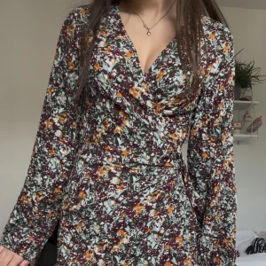 Blommig omlottklänning från MNG - Säljer en blommig omlottklänning från mango i storlek S. Klänningen har långa ärmar, volangdetaljer nertill och knyte i midjan. Perfekt för vår och sommar! Använd 1 gång 