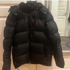 Polo Ralph Lauren jacka - Säljer en svart dunjacka från Polo Ralph Lauren med huva och dragkedja. Har lite små defekter därav priset. Passa på o köp för detta billiga pris istället för en jacka när vinterns kommer för trippla priserna. Ena defekten är osynlig vid användning. Pris kan diskuteras! 