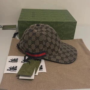 Gucci keps - Snygg keps från Gucci i beige Navy modellen med klassiskt GG-monogram över hela ytan. Kepsen har en röd och blå rand på sidan och justerbar rem baktill. Materialet är canvas med detaljer i svart och insida i mörkt tyg.