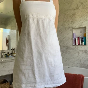 Vit kortklänning med breda axelband - Säljer en enkel och stilren vit klänning med breda axelband och rak halsringning. Klänningen är kort och har en lätt A-linjeformad siluett, perfekt för varma dagar. Köpte den second hand men den har inga defekter så den känns som ny. Klänningen är i linne och är från Uniqlo.💕