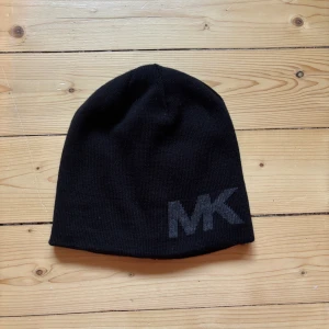 Svart mössa från Michael Kors - Snygg svart mössa från Michael Kors med diskret MK-logga framtill. Enkel och stilren design som passar till det mesta. Tillverkad i mjukt material som håller dig varm under kyliga dagar.