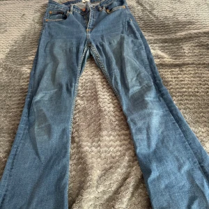 Blå Snake Flare jeans från 157 - Ett par blå Snake Flare jeans från 157 med klassisk femficksdesign och utsvängda ben. Jeansen har normal passform och är tillverkade i ett mjukt denimtyg. Perfekta för dig som gillar retroinspirerad stil.