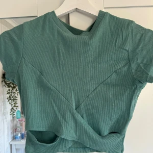 Grön ribbad croppad t-shirt från Pink Woman - Säljer en grön croppad t-shirt från Pink Woman i ribbat material. T-shirten har korta ärmar och en rund halsringning. Perfekt för en avslappnad och trendig stil.