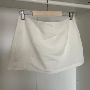 Vit kort kjol med insydda shorts - Vit kort kjol med insydda shorts. Skitsnygg men aldrig använt då jag köpte en i svart också. Så söt och skön med shortsen. Ostretchig med en zip på sidan. Lowwaist!! Den är S men passar mig som oftast har M i underdelar