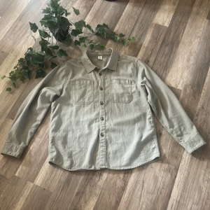Beige skjorta från Lindex Kids - Stilren beige skjorta från Lindex Kids i storlek 164. Skjortan har två bröstfickor, klassisk krage och knäppning framtill. Perfekt för dig som gillar en enkel och clean look. Långärmad och i mjukt bomullstyg.