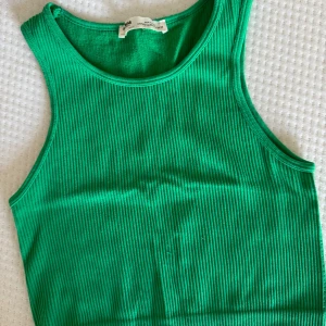Grön ribbad linnetopp från Pull&Bear - Snygg grön ribbad linnetopp från Pull&Bear. Modellen är ärmlös med rund halsringning och croppad passform.