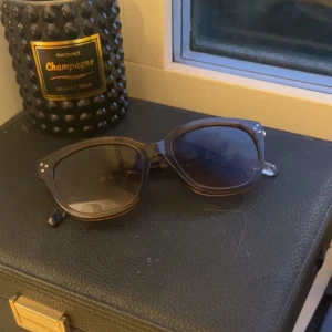 Svarta cat-eye solglasögon - Snygga svarta solglasögon med cat-eye form och transparenta detaljer. Bågarna har en cool, lätt glansig finish och små silvriga prickar vid gångjärnen. Perfekta för att lyfta din stil med en touch av retrovibe.