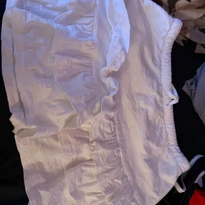 Vit volangkjol i bomull - Supersöt vit kortkjol med volanger och resår i midjan. Kjolen är gjord i ett lätt bomullstyg som känns luftigt och fräscht. Perfekt för varma dagar när du vill ha en chill och trendig look. Passar lika bra med sneakers som sandaler.