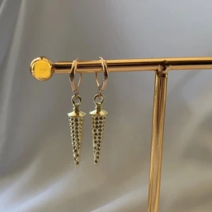 Guldiga konformade örhängen - Snygga guldiga örhängen med konformade hängen som har små nitar längs hela ytan. De hänger i små ringar och ger en cool och edgy vibe till din stil. Perfekta för dig som vill sticka ut lite extra.