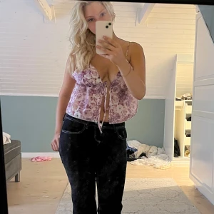 Ljuslila blommig linnetopp med knyt - Supersöt ljuslila linnetopp med blommigt mönster och tunna axelband. Toppen har v-ringning och knyt framtill, vilket ger en avslappnad och trendig look. Perfekt för varma dagar och somriga outfits.