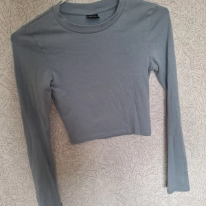 Ljusblå croppad långärmad topp Gina Tricot - Säljer en ljusblå croppad långärmad topp från Gina Tricot i storlek XS. Enkel och stilren design med rund halsringning och mjukt bomullsmaterial. Perfekt att matcha med höga jeans eller kjol för en clean look.