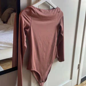 Rostbrun långärmad body från H&M XS - Säljer en stilren rostbrun body från H&M i storlek XS. Bodyn har långa ärmar, rundad hals och knäppning med två tryckknappar nedtill. Tillverkad i mjukt och stretchigt syntetmaterial som sitter tight och bekvämt.