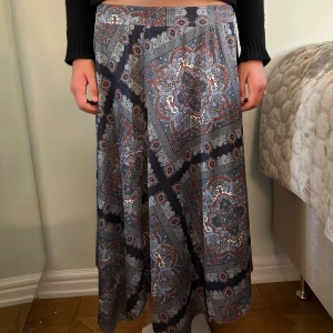 Mönstrad långkjol i blått och rött - Säljer en flowy långkjol med snyggt paisleyinspirerat mönster i blått, grått, rött och vitt. Kjolen har en vid passform och faller snyggt längs benen.