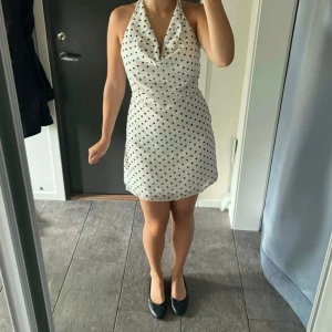 Prickig halterneckklänning - Supersöt kort vit klänning med prickar och halterneck. Klänningen har öppen rygg och knyts i nacken. Aldrig använd💕