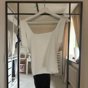 Vit trendigt ZARA  linnetopp med knytband  - Superfin vit linnetopp från Zara med breda axelband som knyts i rosetter. Toppen har rak passform och fyrkantig ringning, vilket ger en clean och modern look. Perfekt till jeans eller kjol för en fräsch sommarstil. Storlek XS o är som nytt. 