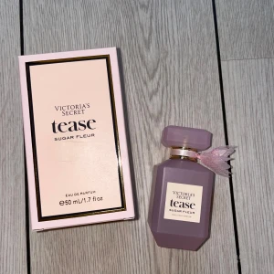 Victoria's Secret Tease Sugar Fleur 50ml - Söt och feminin parfym från Victoria's Secret, Tease Sugar Fleur. Flaskan är matt ljuslila med guldiga detaljer och en rosa rosett vid halsen. Kommer i en matchande ljusrosa kartong med svarta och guldiga kanter. Volym: 50 ml Eau de Parfum. HELT OANVÄND! 
