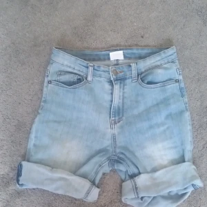 Ljusblå jeansshorts från UNIQ dnm - Snygga ljusblå jeansshorts från UNIQ dnm med klassisk femficksmodell och uppvikta benslut. Shortsen har hög midja, bälteshällor och dragkedja med knapp framtill. 