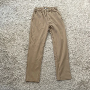 Beiga mjukisbyxor med snörning - Snygga beiga mjukisbyxor med elastisk midja och snörning. Byxorna har raka ben och sidofickor, perfekta för en chill och avslappnad stil. Tillverkade i mjukt material som känns skönt mot huden.