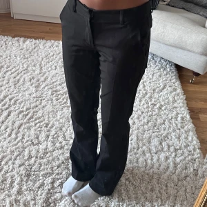 Svarta kostymbyxor från BikBok - Snygga svarta kostymbyxor från BikBok i klassisk rak modell. Byxorna har hällor för bälte, diskreta fickor och stängs med dragkedja och knapp. Perfekta för en clean och stilren look. Materialet känns mjukt och följsamt.