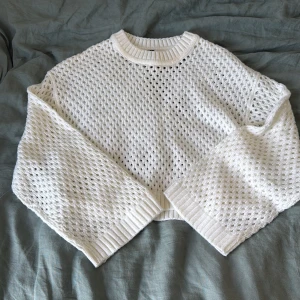 Vit stickad croppad tröja H&M - Säljer en vit stickad tröja från H&M i croppad modell. Tröjan har ett luftigt hålmönster, breda ärmar och ribbade muddar vid hals, ärmslut och nederkant. Perfekt för lager-på-lager och en chill vibe.