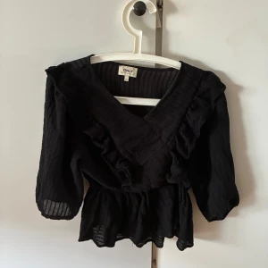 Svart blus med volang från ONLY - Svart blus från ONLY med v-ringning och volangdetaljer längs framsidan och axlarna. 