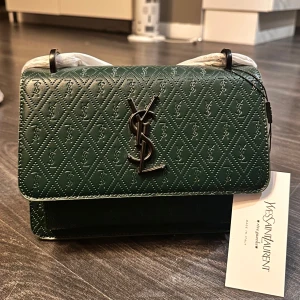 Ysl axelremsväska grön  - Snygg Saint Laurent väska med YSL loggan framtill. Väskan är en replic, men fortfarande väldigt fin i modellen och färgen. Oanvänd med skyddsplasten kvar på remmen. Rymlig och får plats med mobil smink kort osv.🤍 pris kan diskuteras 