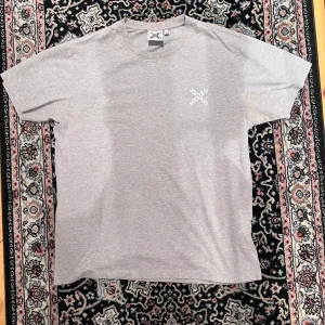 Grå t-shirt från Kenzo i bomull - Snygg grå t-shirt från Kenzo med diskret logga tryckt på bröstet. Klassisk passform med rund hals och korta ärmar. Tillverkad i mjuk bomull som känns skön mot huden. Perfekt för en clean och stilren look.