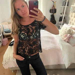 Svart spetsblus med kort ärm - Säljer en svart blus i genombruten spets med snyggt virkat mönster. Modellen är croppad och har korta ärmar samt rund halsringning. Perfekt att styla med jeans eller kjol för en cool look.