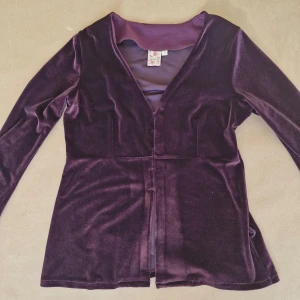Lila sammetstopp från Indiska - Vacker mörklila tröja i sammetstyg från Indiska. Tröjan är långärmad och har v-ringning med resår vid handlederna. Stängs ner till naveln med korsettliknande spännen framtill :) Pris är förhandlingsbart och finns även bundlerabatt, 20% rabatt vid köp av 2! 💗