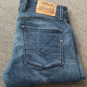 Blå Replay Anbass jeans herr 32/32 - Säljer ett par snygga Replay Anbass jeans i klassisk blå tvätt. Modellen har smal passform, fem fickor och coola detaljer som Replay-logga på fickan. Jeansen är tillverkade i mjukt denimtyg och passar perfekt till sneakers eller boots.