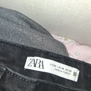 Svarta custum flared jeans från Zara - Svarta jeans från Zara med rak passform och klassisk femficksdesign. Jeansen har råa, fransiga benslut för en trendig look. Tillverkade i ett robust denimtyg som ger en snygg siluett.