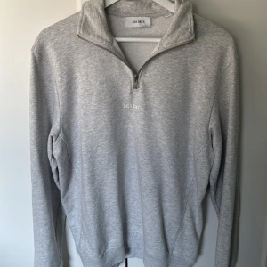 Grå half zip tröja från Les Deux - Snygg grå långärmad tröja från Les Deux med half zip och hög krage. Broderad logga på bröstet och mjukt bomullsmaterial. Perfekt för lager-på-lager och chill dagar.