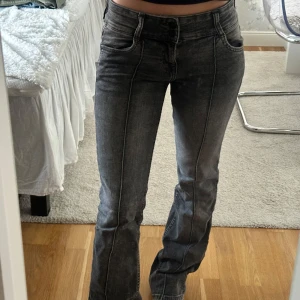 Grå bootcut jeans med hög midja - Säljer ett par grå jeans med snygg tvätt och markerade sömmar. Modellen är bootcut med hög midja och klassiska fickor både fram och bak. Jeansen har en rak passform upptill och lätt utsvängda ben, vilket ger en riktigt trendig siluett.