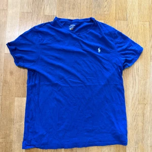 Blå t-shirt från Polo Ralph Lauren - Klassisk blå t-shirt från Polo Ralph Lauren med broderad logga på bröstet. T-shirten är i mjuk bomull, har rund hals och korta ärmar. Perfekt basic-plagg med snygg passform och stilren look.