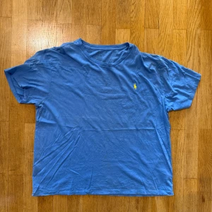 Blå t-shirt från Polo Ralph Lauren - Snygg blå t-shirt från Polo Ralph Lauren med klassisk gul broderad logga på bröstet. T-shirten har rund halsringning och är tillverkad i mjuk bomull. Perfekt basic-plagg med clean look och skön passform.